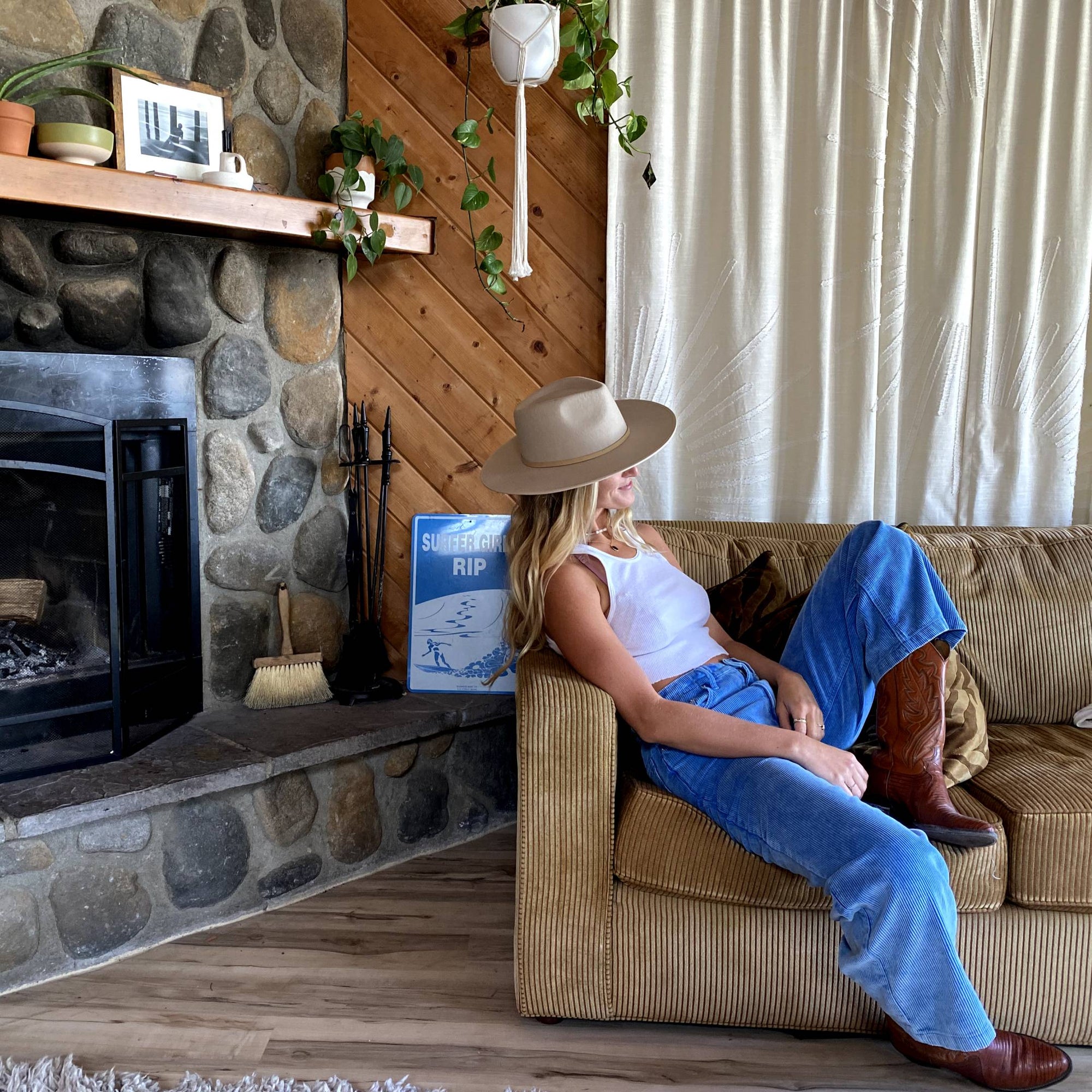 Girl with long hair sitting next to a fireplace with a wide brim hat on